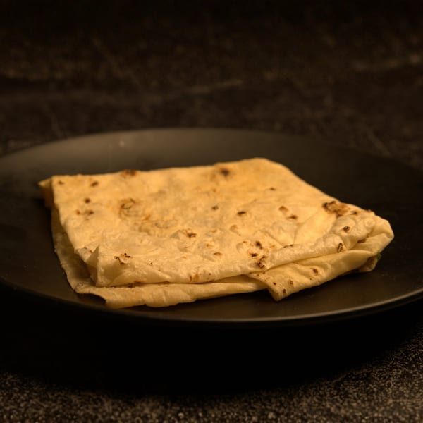 Folded Indian flatbread, likely roti or chapati, with light char marks, on a dark plate.