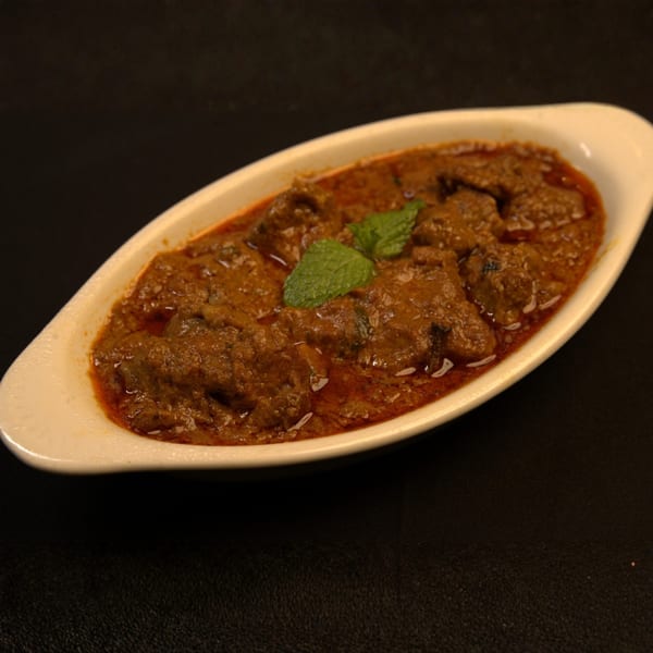 Indian lamb curry with mint garnish in a white oval dish on a dark background.