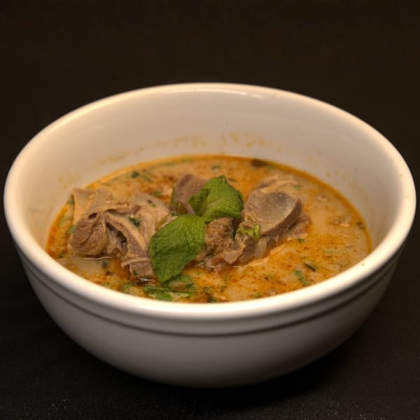 Indian curry with meat pieces and fresh mint leaves in a white bowl on a dark background.