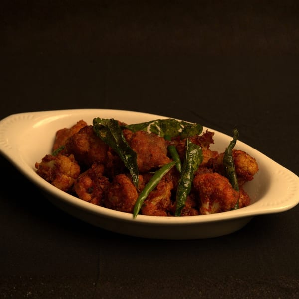 Indian Gobi Manchurian, a fried cauliflower dish, garnished with green chilies and curry leaves in a white bowl.