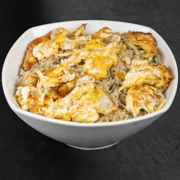 A white bowl filled with Indian-style fried rice topped with scrambled eggs.
