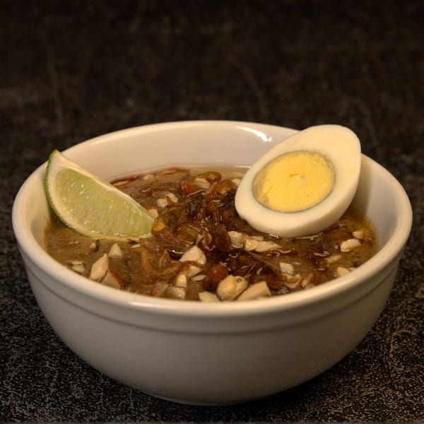 Indian dish with a lime wedge, half a hard-boiled egg, and nuts in a white bowl.