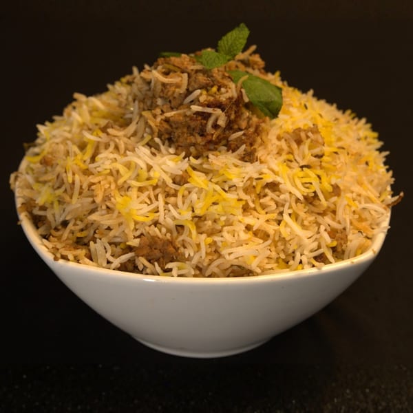 A white bowl filled with Indian biryani, topped with minced meat and fresh mint leaves.