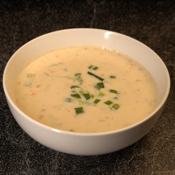 Creamy Indian soup in a white bowl, garnished with chopped green onions, on a dark textured surface.